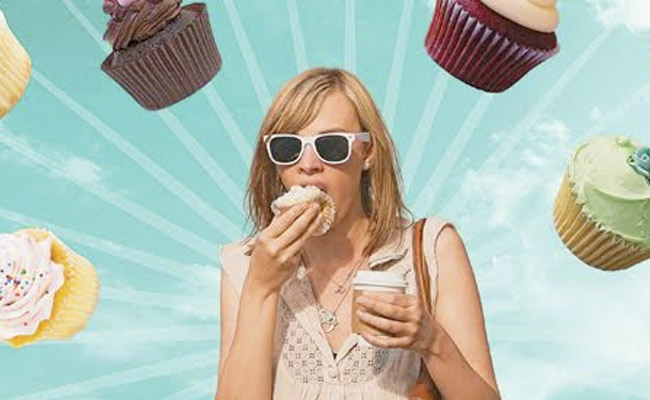 A Brown-haired young woman is experiencing the sweet happiness of cup cakes.